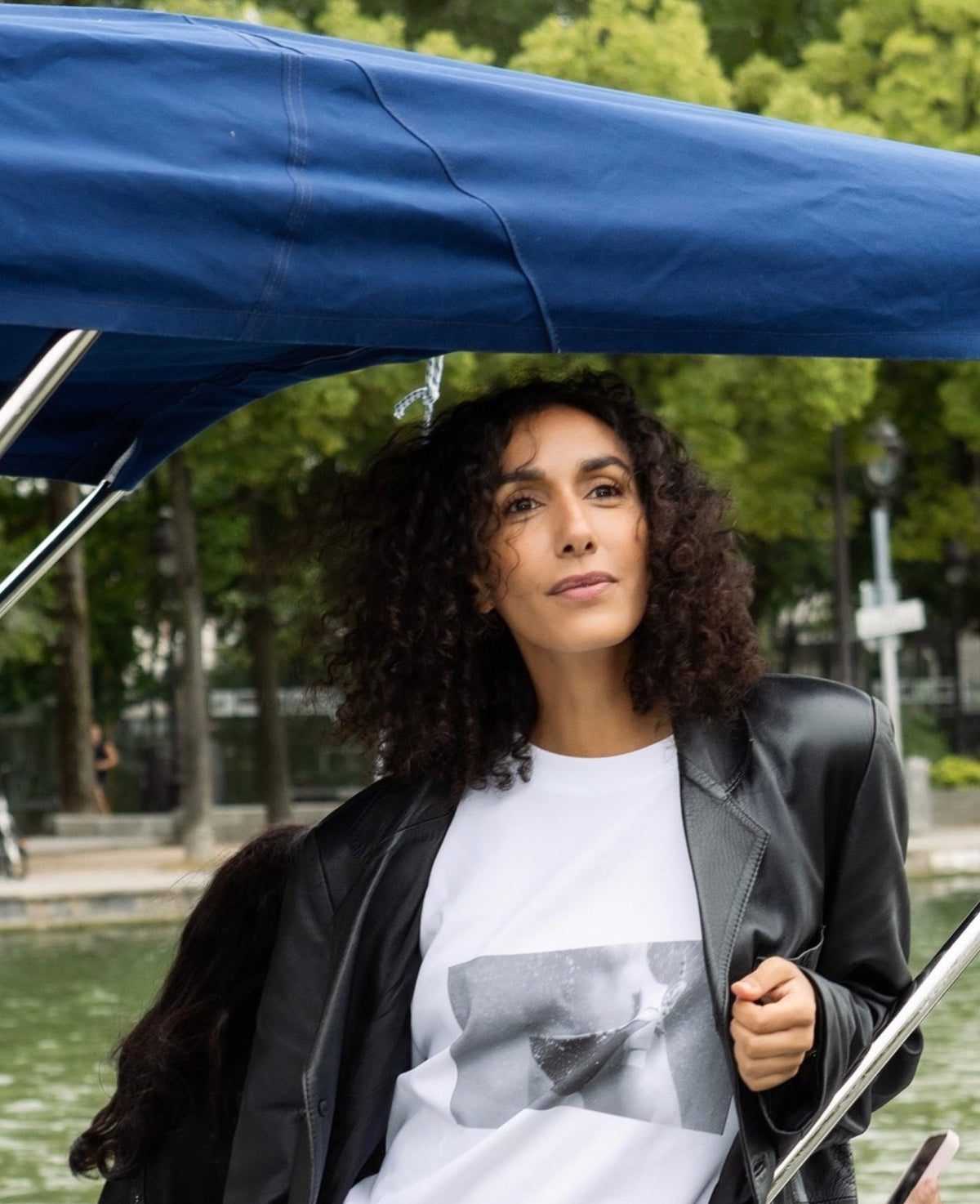 Woman in a black leather jacket under a blue boat canopy beside a canal